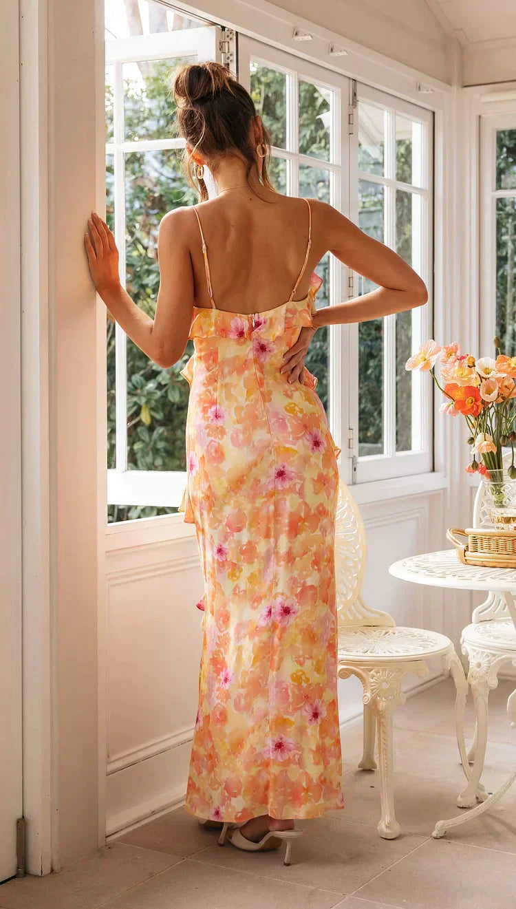 Model draagt een pastel maxi-jurk met ruches, bloemenprint en spaghettibandjes – luchtige en romantische look voor speciale gelegenheden.
