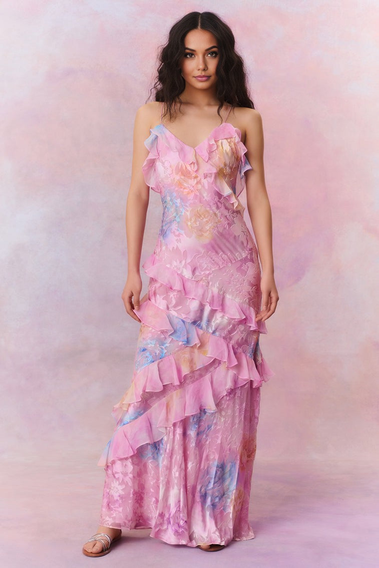 Model draagt een pastel maxi-jurk met ruches, bloemenprint en spaghettibandjes – luchtige en romantische look voor speciale gelegenheden.