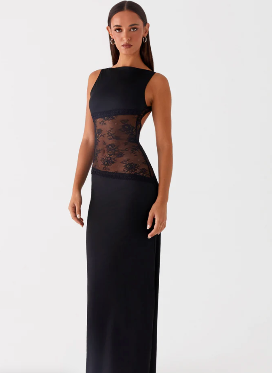 Model draagt een Zwarte maxi-jurk met kanten inzetstuk rond de taille – elegante en moderne avondjurk in een verfijnd ontwerp.