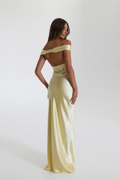 Model draagt een off shoulder satijnen maxi jurk met open rug, perfect voor formele avonden of gala’s.

