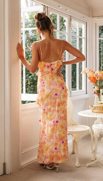 Model draagt een pastel maxi-jurk met ruches, bloemenprint en spaghettibandjes – luchtige en romantische look voor speciale gelegenheden.