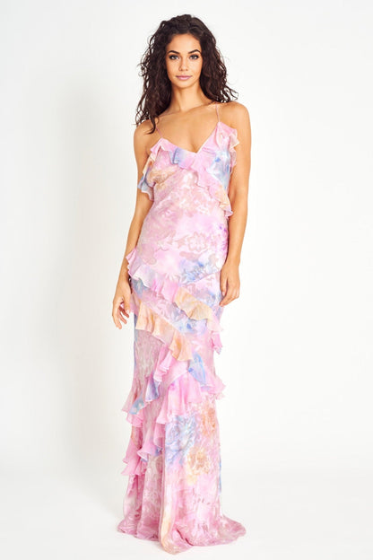Model draagt een pastel maxi-jurk met ruches, bloemenprint en spaghettibandjes – luchtige en romantische look voor speciale gelegenheden.