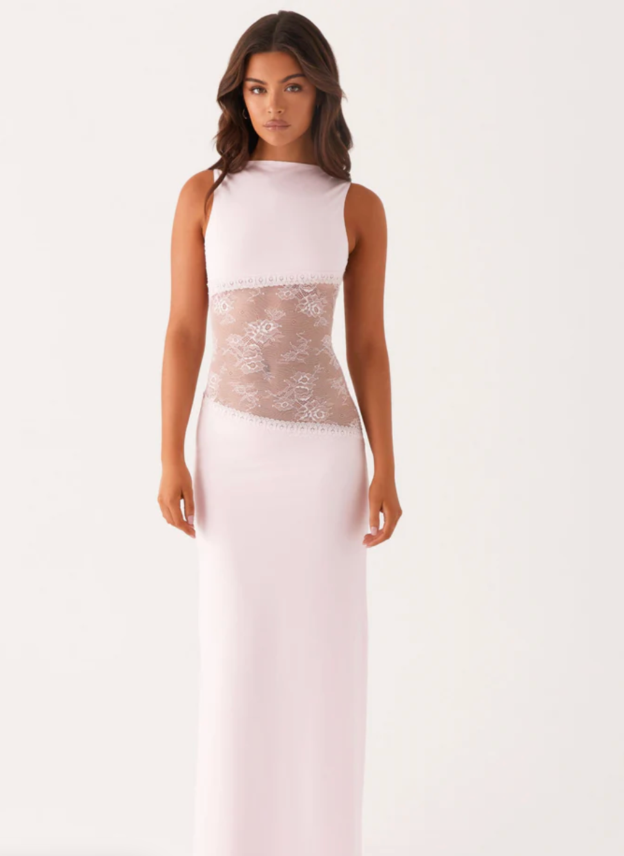 Model draagt een witte maxi-jurk met kanten inzetstuk rond de taille – elegante en moderne avondjurk in een verfijnd ontwerp.