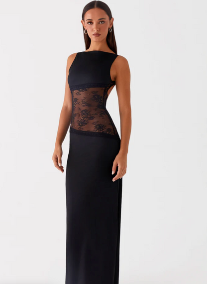 Model draagt een Zwarte maxi-jurk met kanten inzetstuk rond de taille – elegante en moderne avondjurk in een verfijnd ontwerp.