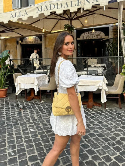 Model draagt een luxe geborduurde bloemenjurk met pofmouwen, een diepe V-hals en een speelse ballonzoom. De jurk heeft verfijnde borduurdetails en een elegante pasvorm, perfect voor zomerse dagen en feestelijke gelegenheden