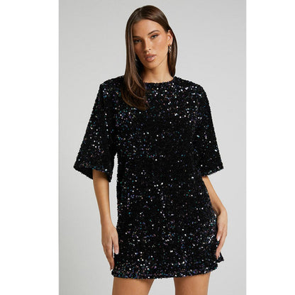 Model draagt een luxe mini-jurk met pailletten in roze en zwart, met korte mouwen en open rug met strikdetail – perfect voor feestelijke gelegenheden of avondjes uit.