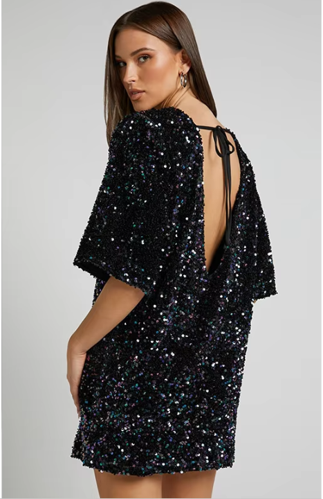 Model draagt een luxe mini-jurk met pailletten in roze en zwart, met korte mouwen en open rug met strikdetail – perfect voor feestelijke gelegenheden of avondjes uit.