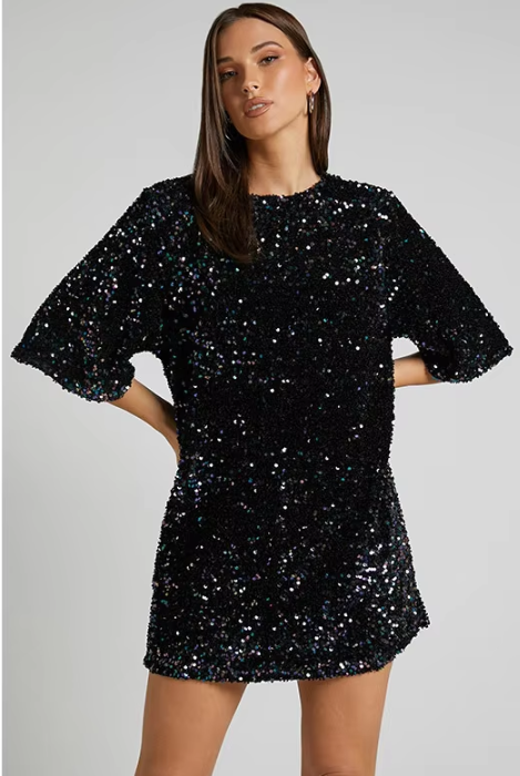 Model draagt een luxe mini-jurk met pailletten in roze en zwart, met korte mouwen en open rug met strikdetail – perfect voor feestelijke gelegenheden of avondjes uit.