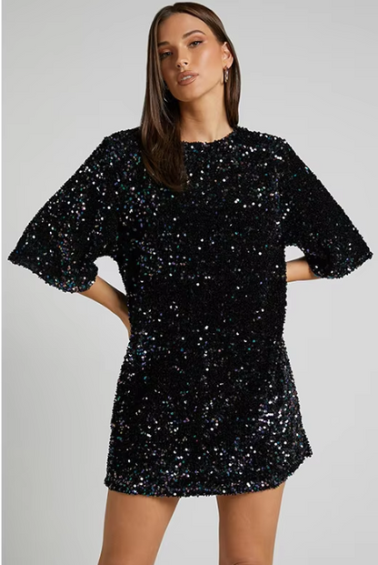 Model draagt een luxe mini-jurk met pailletten in roze en zwart, met korte mouwen en open rug met strikdetail – perfect voor feestelijke gelegenheden of avondjes uit.