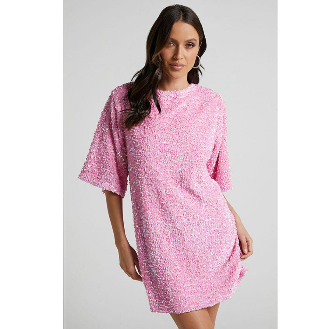vModel draagt een luxe mini-jurk met pailletten in roze en zwart, met korte mouwen en open rug met strikdetail – perfect voor feestelijke gelegenheden of avondjes uit.