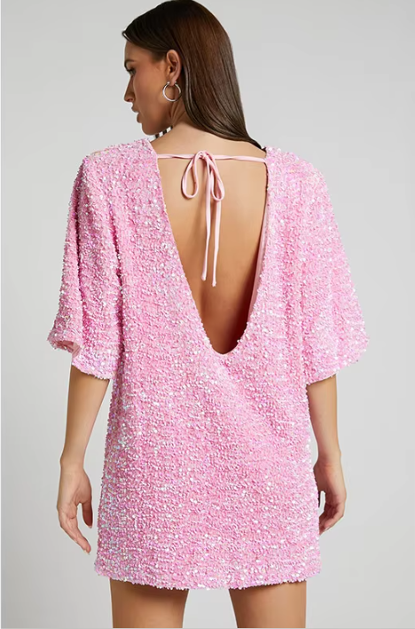 Model draagt een luxe mini-jurk met pailletten in roze en zwart, met korte mouwen en open rug met strikdetail – perfect voor feestelijke gelegenheden of avondjes uit.
