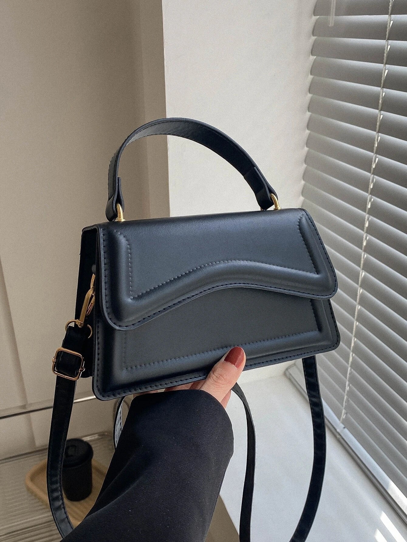 Zwarte minimalistische dames schoudertas met golvend design en verstelbare riem, close-up in hand








