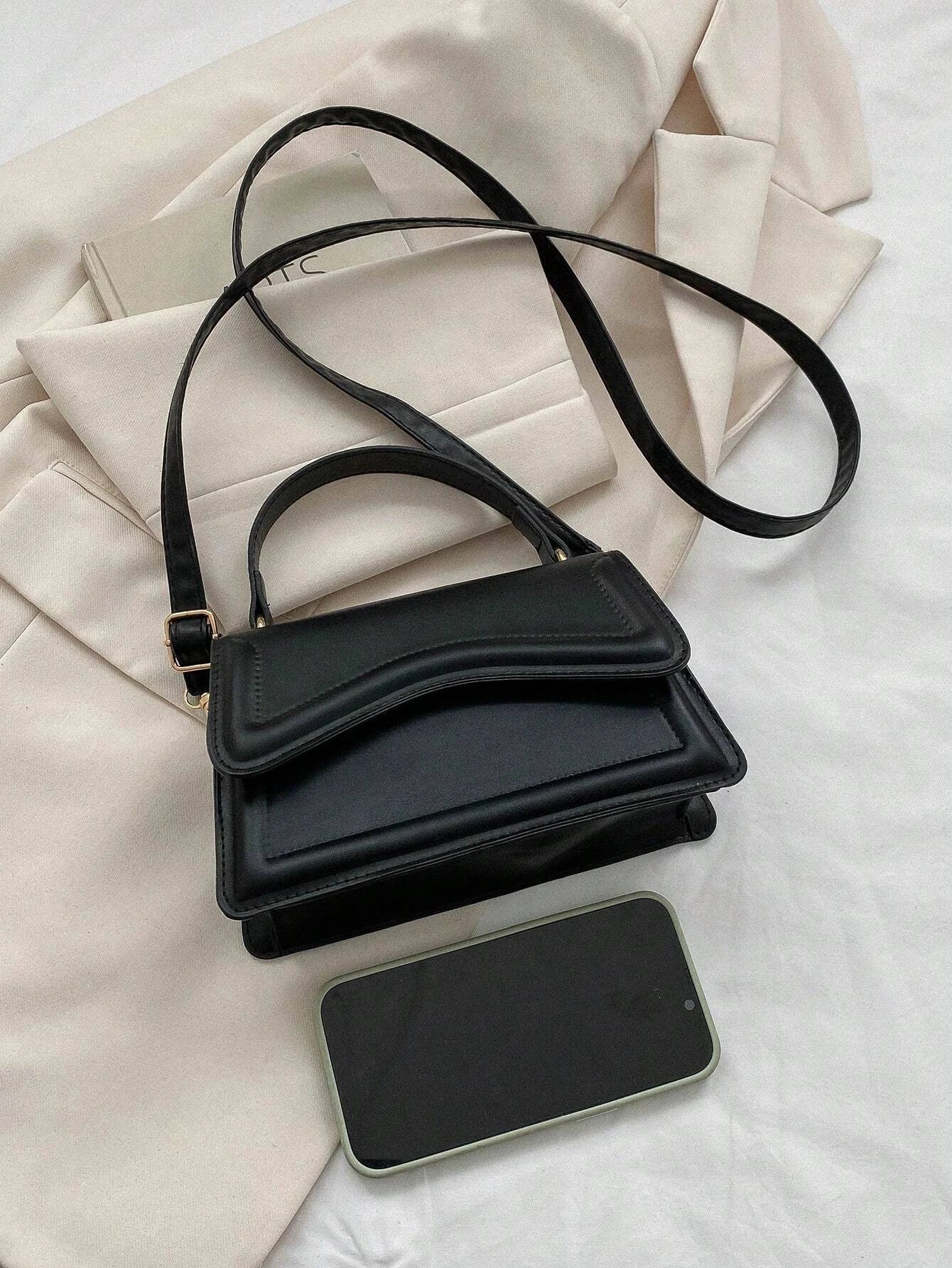 Zwarte minimalistische dames schoudertas met golvend design en verstelbare riem, close-up in hand








