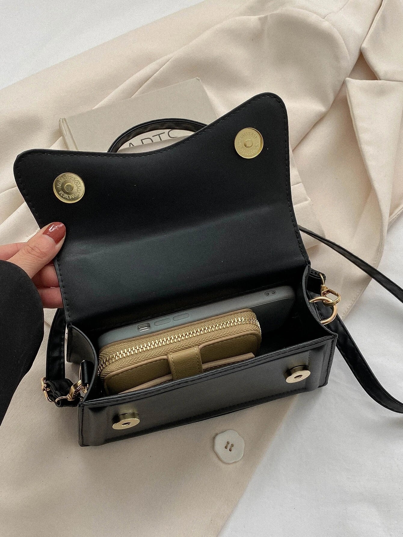 Zwarte minimalistische dames schoudertas met golvend design en verstelbare riem, close-up in hand








