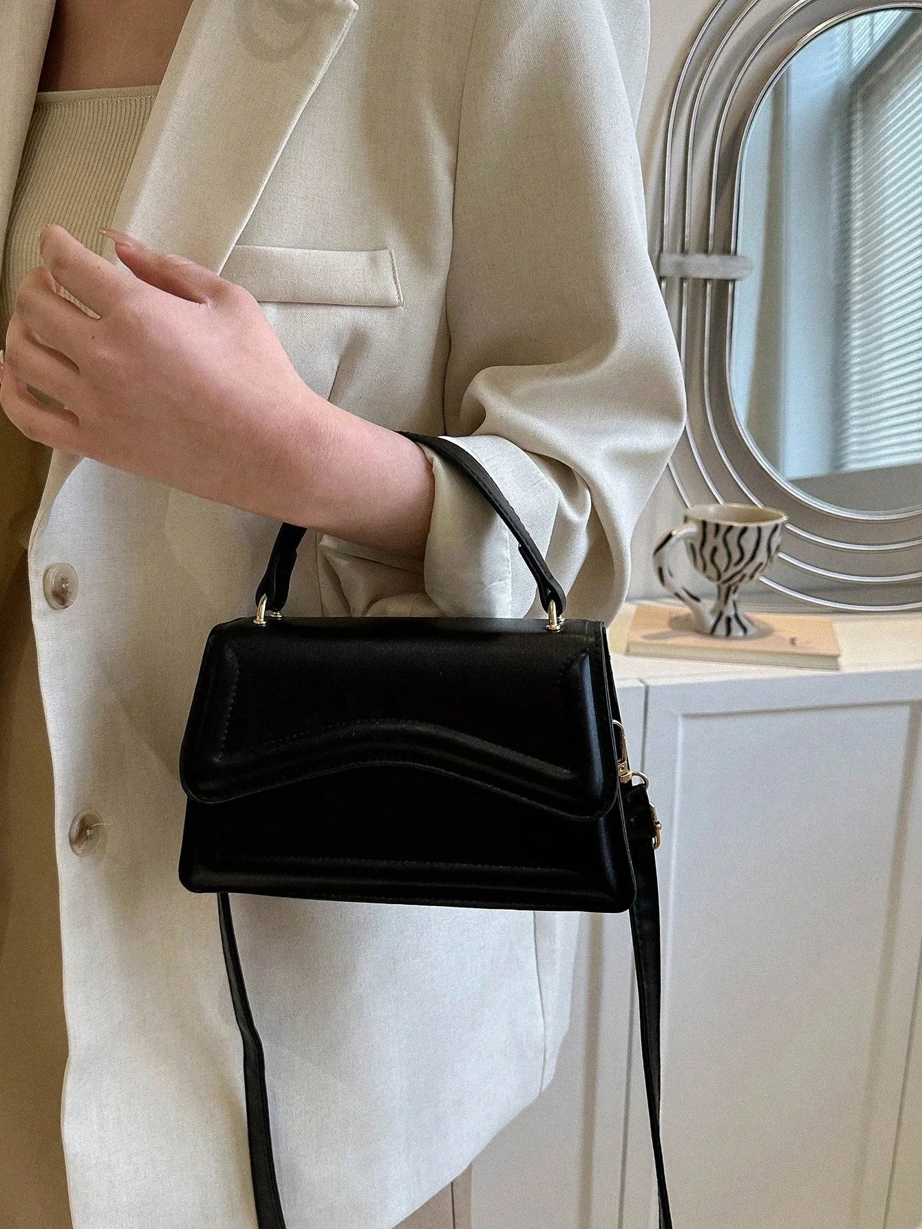 Zwarte minimalistische dames schoudertas met golvend design en verstelbare riem, close-up in hand








