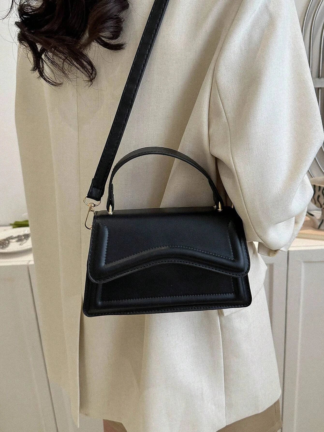 Zwarte minimalistische dames schoudertas met golvend design en verstelbare riem, close-up in hand









