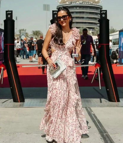 Vrouw draagt een romantische lange zomerjurk met roze bloemenprint, diepe V-hals en hoge split – perfect voor bruiloften of vakanties.