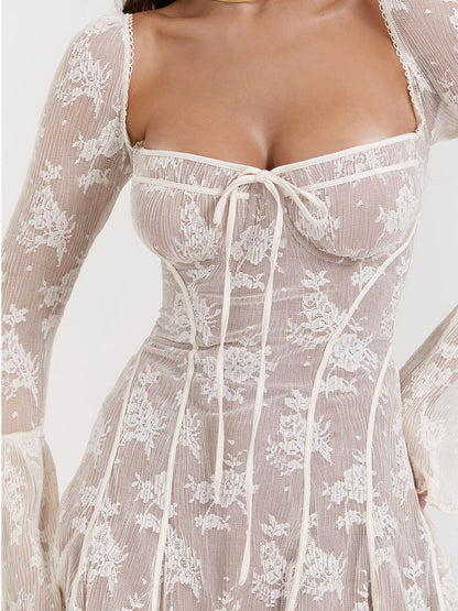 Model draagt een witte kanten mini-jurk met lange mouwen, bloemenmotief en strikdetail – een romantische en elegante outfit voor speciale gelegenheden.








