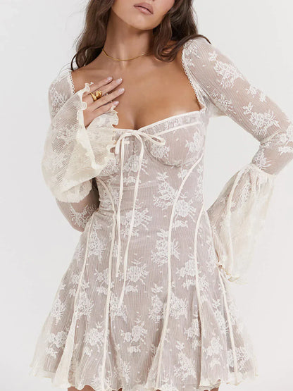 Model draagt een witte kanten mini-jurk met lange mouwen, bloemenmotief en strikdetail – een romantische en elegante outfit voor speciale gelegenheden.








