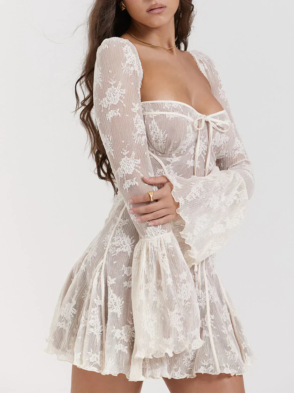 Model draagt een witte kanten mini-jurk met lange mouwen, bloemenmotief en strikdetail – een romantische en elegante outfit voor speciale gelegenheden.








