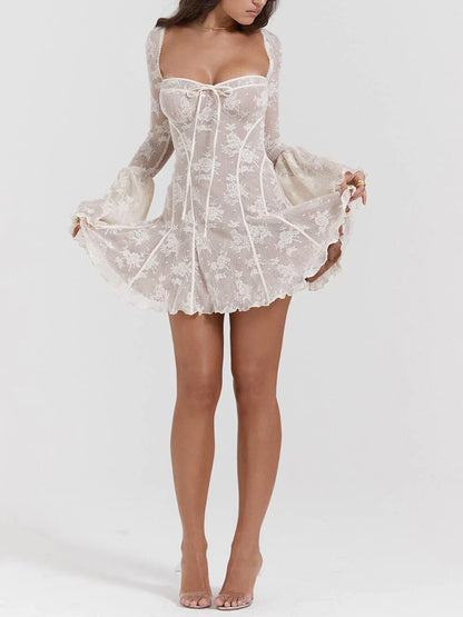 Model draagt een witte kanten mini-jurk met lange mouwen, bloemenmotief en strikdetail – een romantische en elegante outfit voor speciale gelegenheden.








