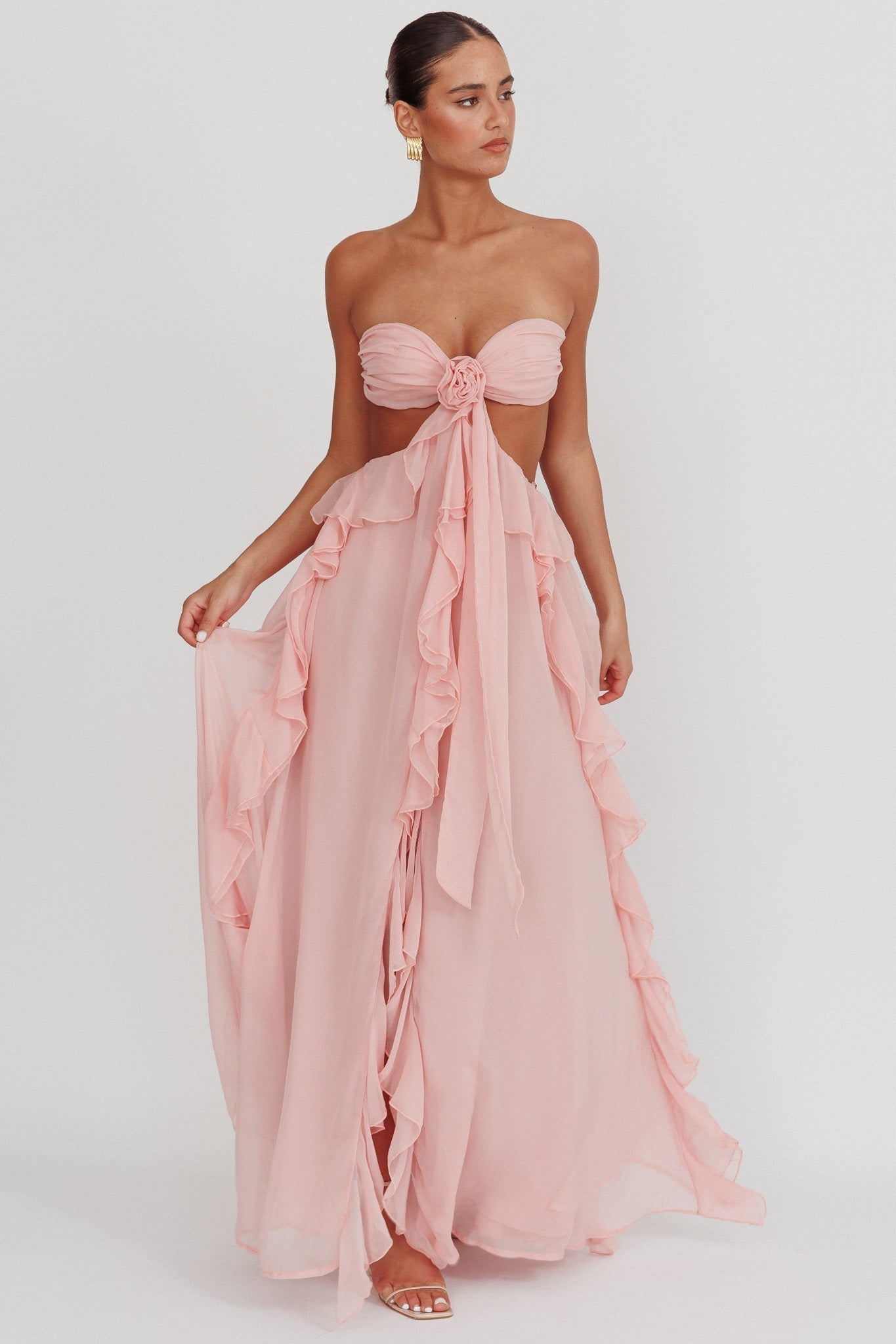 Model draagt een blush roze maxi jurk met ruches, strapless top en open rug, perfect voor zomerse evenementen.