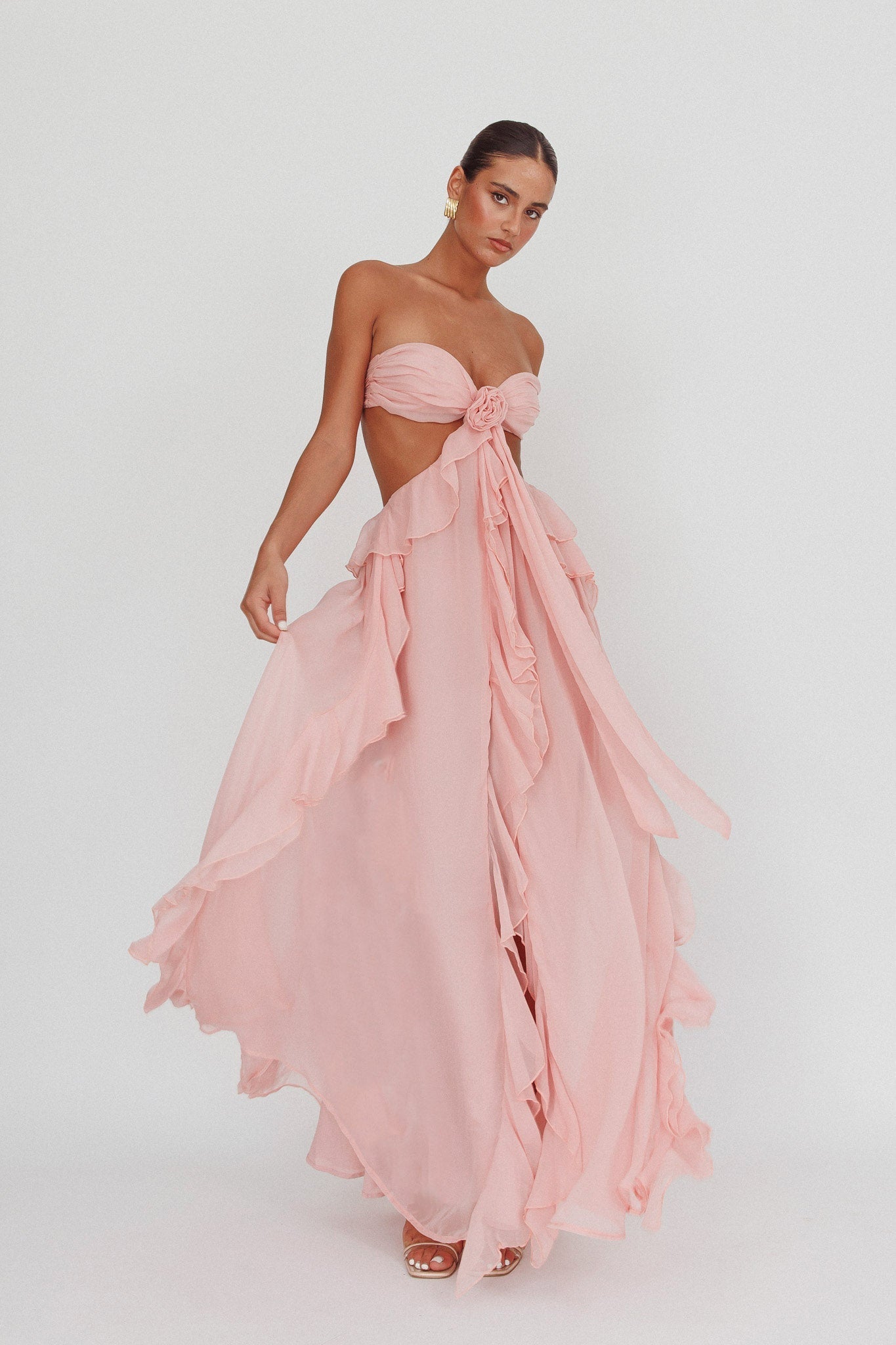 Model draagt een blush roze maxi jurk met ruches, strapless top en open rug, perfect voor zomerse evenementen.