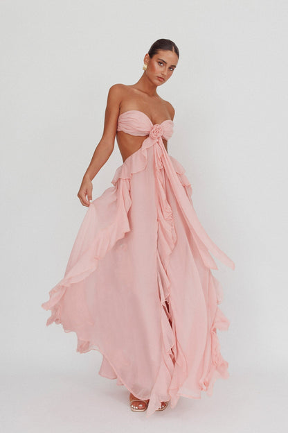 Model draagt een blush roze maxi jurk met ruches, strapless top en open rug, perfect voor zomerse evenementen.