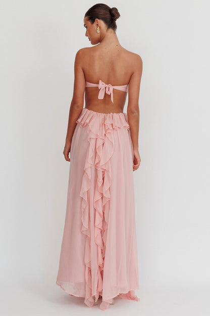 Model draagt een blush roze maxi jurk met ruches, strapless top en open rug, perfect voor zomerse evenementen.