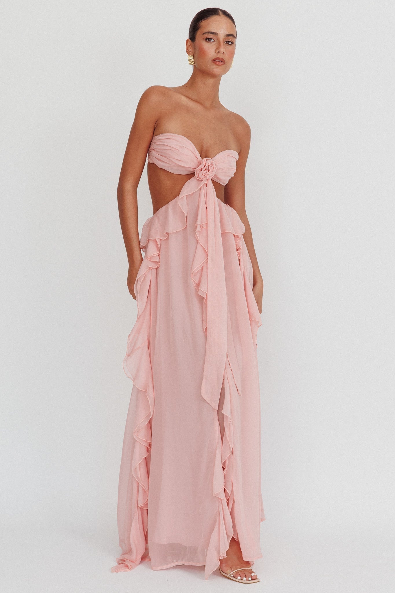 Model draagt een blush roze maxi jurk met ruches, strapless top en open rug, perfect voor zomerse evenementen.