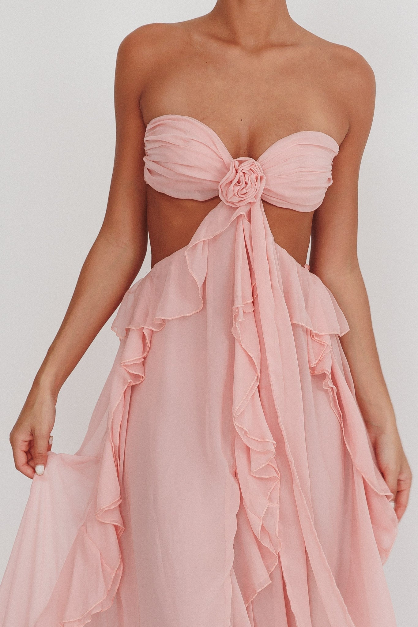 Model draagt een blush roze maxi jurk met ruches, strapless top en open rug, perfect voor zomerse evenementen.