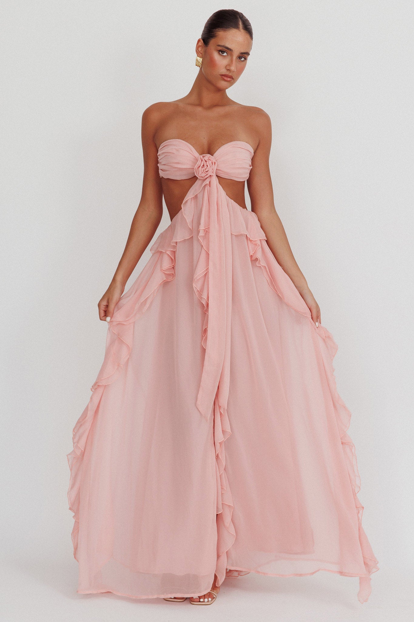 Model draagt een blush roze maxi jurk met ruches, strapless top en open rug, perfect voor zomerse evenementen.