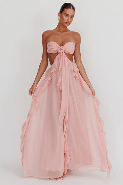 Model draagt een blush roze maxi jurk met ruches, strapless top en open rug, perfect voor zomerse evenementen.